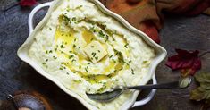 mashed potatoes in a white bowl with butter and parsley on top, next to a spoon