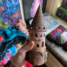 a hand holding up a clay model of a castle in front of a pile of yarn