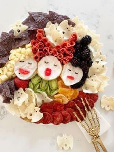 a plate filled with fruit and veggies on top of a white table next to gold utensils