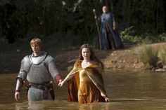 a man and woman in armor walking through water with two other people standing behind them