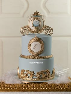 a three tiered blue and gold wedding cake on a table with white furnishing