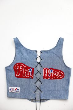 Upcycled Phillies Denim Corset Top. Each top is one of a kind and reworked by hand using denim fabric from jeans and team t-shirts. The back is adjustable. Reworked from Phillies MLB Majestic shirts and jerseys and denim jeans Size Medium THIS ITEM IS REWORKED AND ONE OF A KIND 🔥 ONLY ONE AVAILABLE! ------------------- ☆Tonguetied Apparel creates unique, one-of-a-kind upcycled garments from vintage/thrifted apparel. These thrifted/vintage garments may have some minor damages including small hol Fitted Denim Patchwork Tops, Fitted Denim Tops With Patchwork, Denim Crew Neck Top For Streetwear, Denim Blue Cotton Tops For Streetwear, Casual Upcycled Tops For Streetwear, Casual Upcycled Streetwear Tops, Reworked Fitted Casual Tops, Casual Fitted Reworked Tops, Casual Reworked Tops For Streetwear