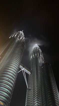 two very tall buildings towering into the sky at night with clouds in the air above them