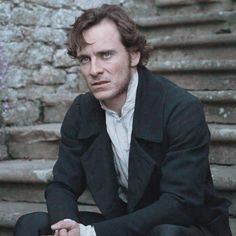 a man sitting on the ground in front of some stone steps with his hands folded