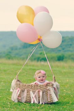 a baby sitting in a basket with balloons attached to the handle, on top of grass