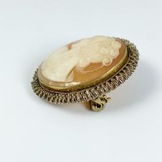 The listing is for a Vintage Cameo Brooch. The design is of a lovely women in profile with flowers in her hair. The cameo is bezel set with a textured wire frame. The cameo has a jump ring in the middle of the back that may have once held a bail for using it on a necklace (this bail can be easily added by a jeweler). The brooch pin is in working condition. Weight: 6.1 grams Marks: unmarked (may be gold filled) Measurements: 1.1692 inches long total and 0.9842 inches at widest. 💕All items in my Cameo Brooches For Wedding, Antique Style Pins As Gifts, Flowers In Her Hair, Vintage Cameo, Dendritic Agate, Cameo Brooch, Oval Rings, Wire Frame, Shell Pendant