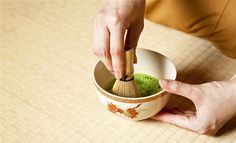 a person holding a wooden spoon in a cup filled with green liquid and broccoli