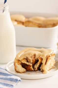 a cinnamon roll with icing on a white plate next to a glass of milk