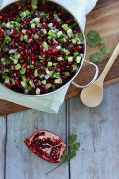 pomegranate and cucumbers in a pot on a wooden cutting board