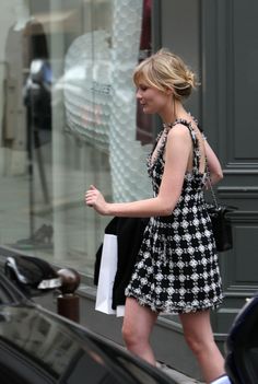 a woman is walking down the street with her hand in her pocket and wearing a black and white dress