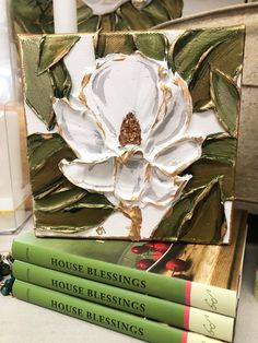 three books stacked on top of each other next to a white flower and green leaves