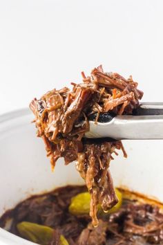 a spoon full of shredded beef and peppers in a white bowl with sauce on the side