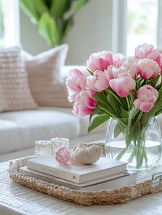 pink tulips in a glass vase on a coffee table with books and candles