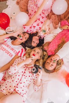 four women laying on the floor with balloons and teddy bears in the background, all wearing matching pajamas