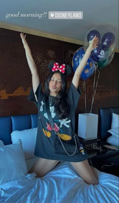 a woman sitting on top of a bed with balloons in the air above her head