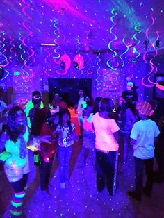 a group of people dancing in a room with purple and blue lights on the ceiling