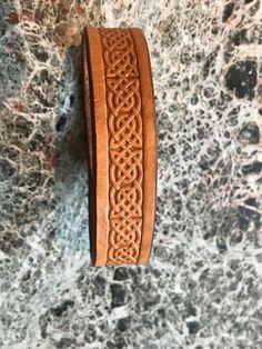 a brown leather bracelet with an intricate design on the outside and inside, sitting on a marble surface