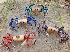 four wine corks with beaded spider decorations on them sitting in the dirt next to grass