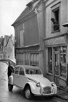 an old car parked in front of a building on the side of a street next to a dog