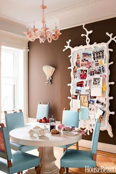 a dining room table with blue chairs next to a white chandelier and pictures on the wall