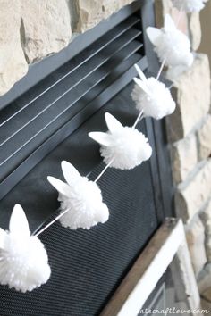 some white paper flowers are hanging from a wire on a fireplace mantel in front of a stone wall