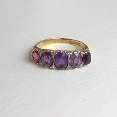 a yellow gold ring with amethyst stones and diamonds on the sides, sitting on a white surface