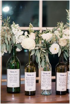 three wine bottles with flowers in them sitting on a table