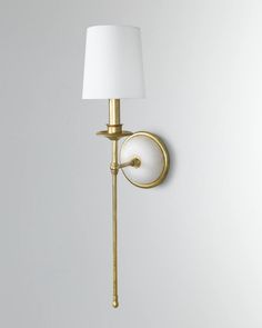 a gold wall light with a white shade on it's side and a lamp plugged into the wall