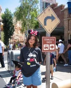 a woman standing next to a street sign with minnie mouse ears on it's head