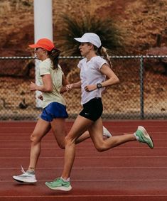 two women running on a track with one wearing an orange visor and the other in blue