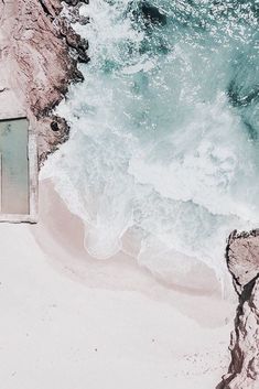 an aerial view of the ocean with waves crashing on the shore and people standing in the sand