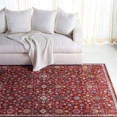 a red rug with white pillows on top of it and a couch in the background