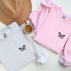 two sweaters and a hat sitting next to each other on a white table with a cup of coffee