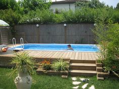 a person swimming in a backyard pool with steps leading up to the decking area