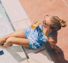 a woman sitting next to a swimming pool drinking from a beverage glass in her hand