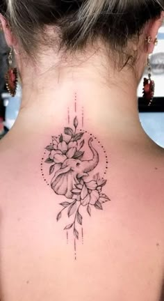 the back of a woman's neck with an elephant and flowers tattoo on it