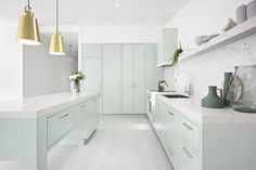 a kitchen with white counter tops and light green cabinets, along with gold pendant lights hanging from the ceiling