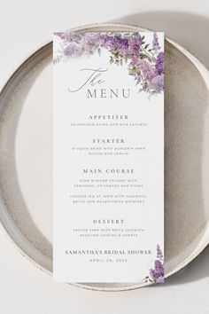 a plate with a menu on it and purple flowers in the center, sitting on top of a white table cloth