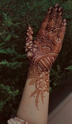 a woman's hand with henna on it and some trees in the background