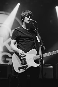 a young man holding a guitar while standing in front of a microphone