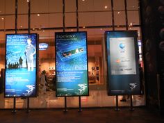 three large signs in front of a building with people walking past them at night time