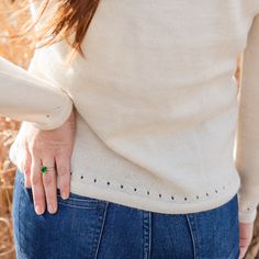 a woman with her hand on the back of her stomach, wearing a white sweater and blue jeans