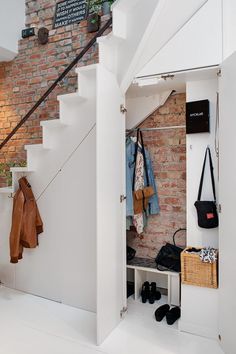 a room with some clothes hanging on the wall next to a stair case and coat rack