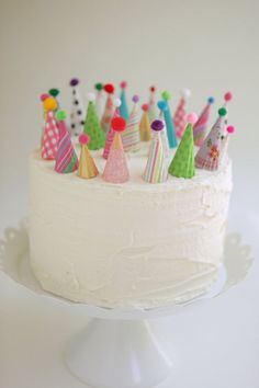 a cake with white frosting topped with lots of small colorful birthday hats on top