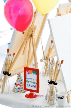 a birthday party with balloons and pictures on easel stands in front of an easel