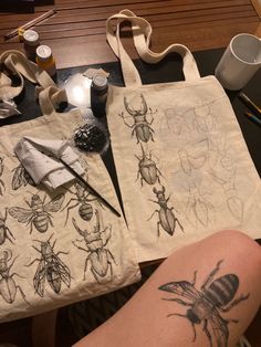 two tote bags with drawings of bugs on them next to a person's legs