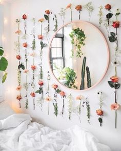 there is a mirror with flowers on the wall and plants hanging from it's sides