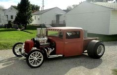 an old red car is parked on the side of the road in front of some houses