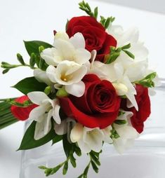 red and white flowers are arranged in a bouquet on a clear glass vase with greenery