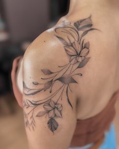 the back of a woman's shoulder with flowers and leaves tattooed on her arm